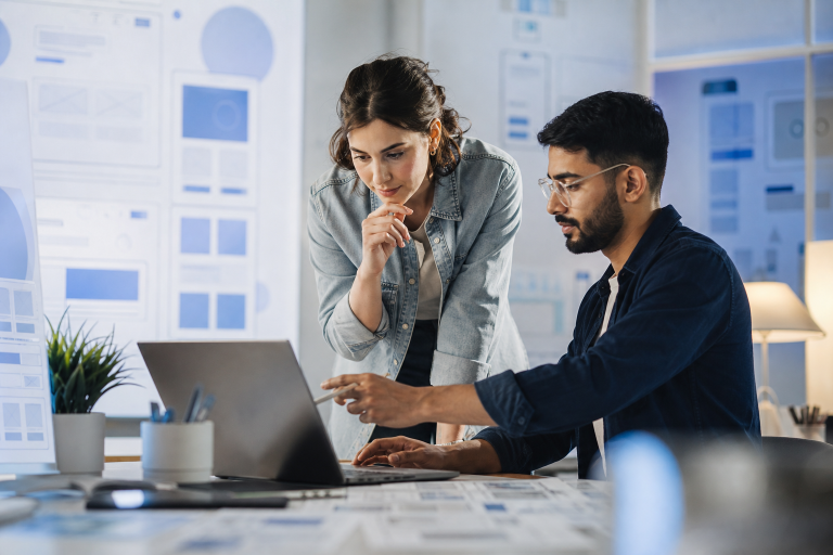 Designer and developer collaborating on a Webflow website strategy with wireframes and component layouts on a modern desk